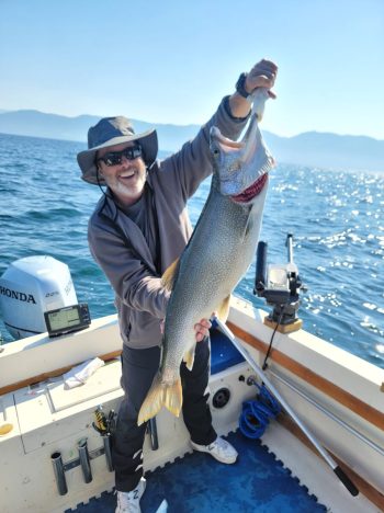 A man standing on a boat holding a Trout he caught a Flathead Lake Charters.